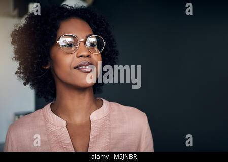 Smiling young African businesswoman wearing glasses à profondément dans ses pensées alors qu'il se trouvait seul dans un bureau moderne Banque D'Images