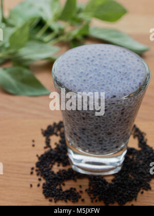 Gonflé ou basilic graines sabja en verre avec les graines et les feuilles sur fond de bois Banque D'Images