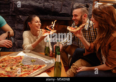 Smiling friends having fun à la maison tandis que le grillage de la bière et manger des pizzas Banque D'Images