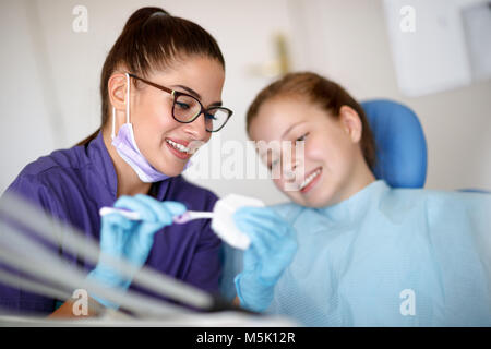 Femme dentiste sur dents modèle montre à la fille en fauteuil dentaire comment bien se brosser les dents Banque D'Images