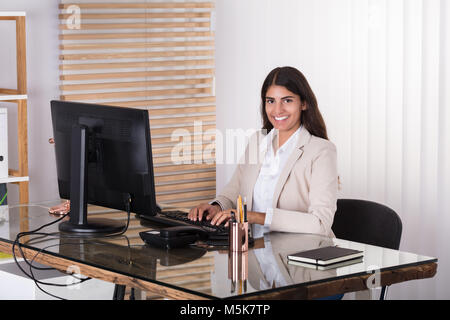 Les jeunes de taper au clavier Smiling Businesswoman In Office Banque D'Images