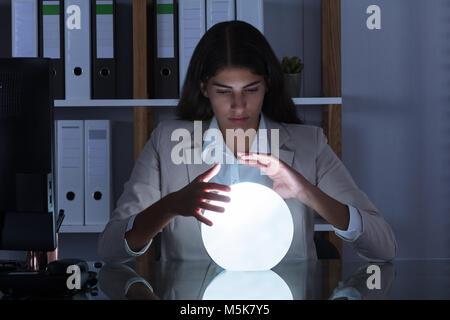 Surchargés de Young Businesswoman Looking dans l'avenir dans une boule de cristal In Office Banque D'Images