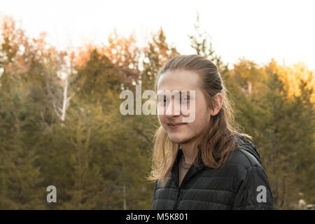 Portrait d'un jeune homme aux cheveux longs avec des arbres en arrière-plan ; la fin de l'après-midi, coucher du soleil Banque D'Images