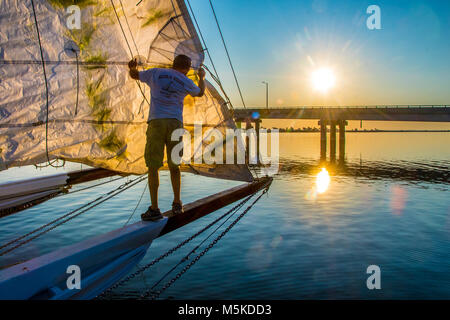 Correctifs de mâles adultes voile sur bateau bonite traditionnels comme le soleil se lève au-dessus d'un pont dans la distance, l'Île de faire face, au Maryland. Banque D'Images