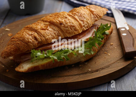 Sandwich croissant au jambon et salade sur une planche à découper en bois Banque D'Images