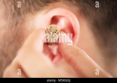 Close-up d'une personne qui met de l'aide auditive sur l'oreille de l'Homme Banque D'Images