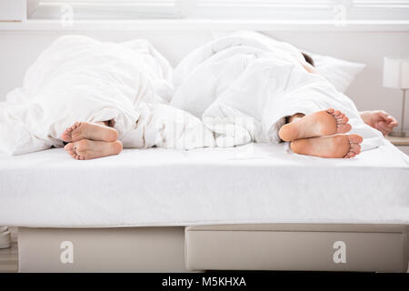 Photo de couple au lit sous les draps Banque D'Images
