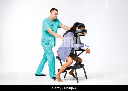 Massage thème et bureau. Costume bleu avec un thérapeute de sexe masculin faisant massage du dos et du cou pour les jeunes femme, femme d'affaires en chemise sur un fauteuil de massage s Banque D'Images