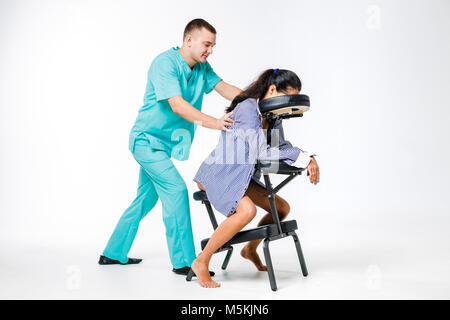 Massage thème et bureau. Costume bleu avec un thérapeute de sexe masculin faisant massage du dos et du cou pour les jeunes femme, femme d'affaires en chemise sur un fauteuil de massage s Banque D'Images