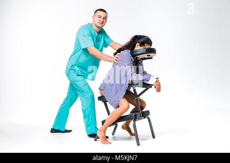 Massage thème et bureau. Costume bleu avec un thérapeute de sexe masculin faisant massage du dos et du cou pour les jeunes femme, femme d'affaires en chemise sur un fauteuil de massage s Banque D'Images