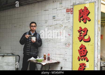 Un homme est en train de manger ses nouilles à côté d'un magasin dans une ruelle à Hong Kong Banque D'Images