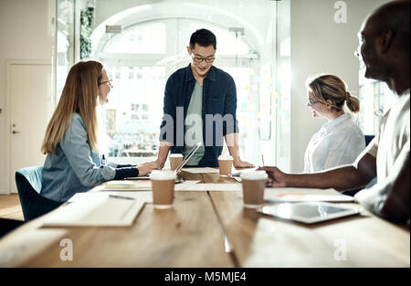 Happy manager debout à une table d'une réunion avec divers collègues tout en travaillant ensemble dans un bureau moderne Banque D'Images