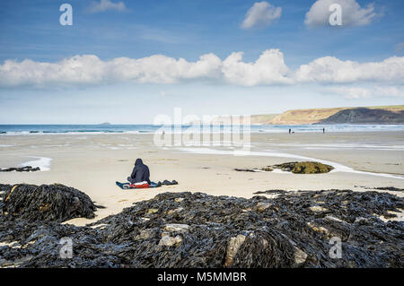 Une silhouette encapuchonnée assise sur la plage de Sennen Cove à Cornwall. Banque D'Images