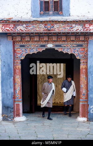 Trongsa, Bhoutan. Deux jeunes hommes en tenue traditionnelle (GHO) Entrer dans la première Cour de Trongsa Dzong (Monastery-Fortress), vue de l'intérieur de la Banque D'Images