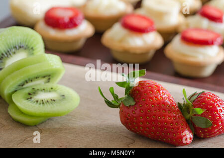 Fraise et kiwi à l'avant, petites tartelettes décorées avec de la crème rempli. Banque D'Images