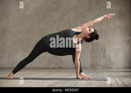 Jeune femme pratiquant le yoga, faire Utthita parsvakonasana, exercice posent l'angle de côté, le travail, le port des vêtements de sport, pantalon noir et haut, dans Banque D'Images