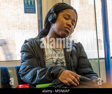 Jeune femme noire passager, somnolant sur un train de tube tout en écoutant de la musique avec des écouteurs. Angleterre, Royaume-Uni. Banque D'Images