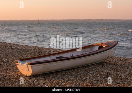 Un voile aviron canot tiré vers le haut sur la plage et se reposer sur une banque de bardeaux sur plage de galets au coucher du soleil. Paysage côtier avec seascape boat on beach. Banque D'Images