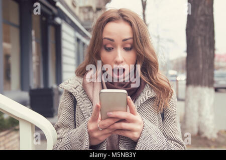 SMS. Funny choqué impatient girl looking at phone voir mauvaises nouvelles photos message avec expression visage surpris sur la rue de la ville historique. Banque D'Images
