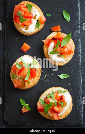 Bruschetta italienne et concassé de tomates, basilic, mozzarella et de vinaigre balsamique. Des crostini ou bruschetta caprese sur ston noir Banque D'Images