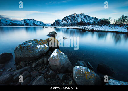 Le lac encore avec de grosses roches avec des plaques de neige et les montagnes enneigées en arrière-plan Banque D'Images