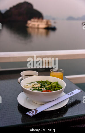 Petit déjeuner matinal composé de jus d'orange, de café et d'un bol de soupe de poulet et de nouilles de riz à bord d'un bateau de croisière de luxe sur Halong Bay Banque D'Images