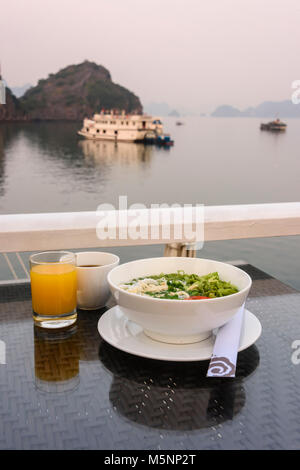 Tôt le matin, petit-déjeuner composé de jus d'orange, café et un bol de soupe aux nouilles poulet et ric à bord d'un navire de croisière de luxe sur la baie d'Halong Banque D'Images