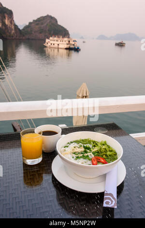 Tôt le matin, petit-déjeuner composé de jus d'orange, café et un bol de soupe aux nouilles poulet et ric à bord d'un navire de croisière de luxe sur la baie d'Halong Banque D'Images