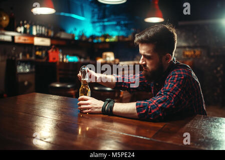 Triste homme assis au bar comptoir et ouvre la bouteille avec de l'alcool des boissons. Personne de sexe masculin dans la pub, l'alcoolisme Banque D'Images