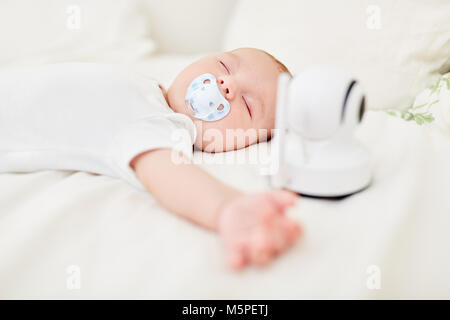 Bébé avec tétine en bouche avec moniteur bébé dort paisiblement sur lit bébé Banque D'Images