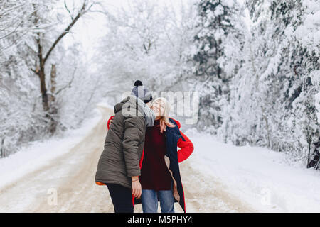Une belle famille couple en train de marcher sur une route enneigée dans les bois et des caresses, des baisers Banque D'Images