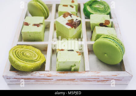 Des macarons colorés dans panier en osier avec poignées avec petites fleurs blanches sur fond de bois. Focus sélectif. Banque D'Images