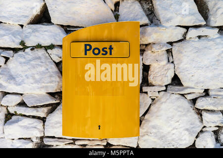 Post box jaune sur Gray Stone Fence. Banque D'Images