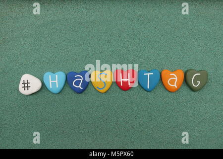 Hashtag mot composé avec coeur multicolore pierres sur sable vert Banque D'Images