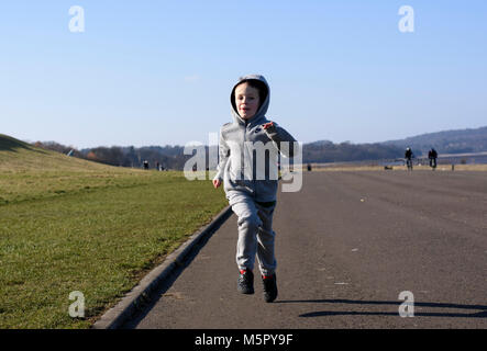 Un garçon de six ans courir avec son capot sur un jour d'hiver ensoleillé Banque D'Images