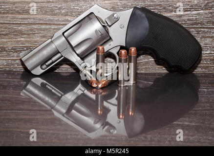 Un revolver Magnum 357 acier inoxydable avec cinq balles en face de lui avec un fond de bois et de tous les sur une surface réfléchissante Banque D'Images