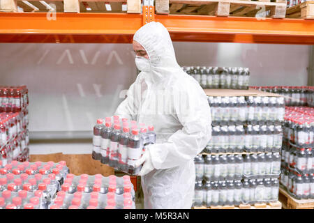 Voir le profil de travailleur homme porter combinaison et masque de sécurité transportant des bouteilles de boissons gazeuses en plastique alors que l'accent sur le chargement de marchandises, de l'intérieur de f Banque D'Images