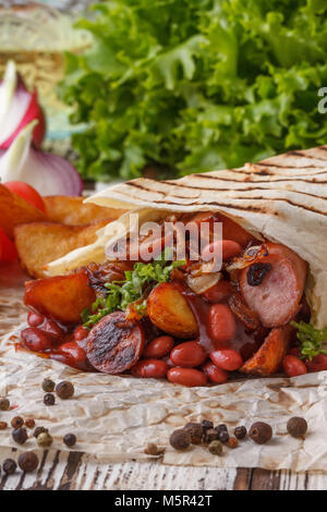 Shaurma original et robuste avec des haricots et des saucisses. La nature morte sur un fond de bois. Banque D'Images