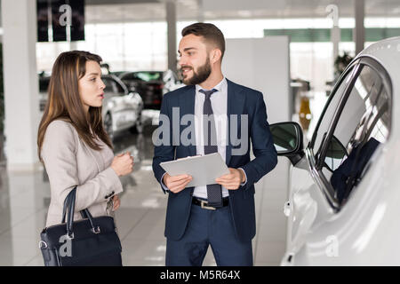 Portrait of handsome car salesman talking to young woman helping her choisissez luxury car in showroom Banque D'Images