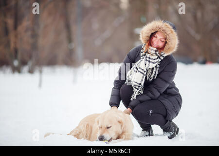 La photo d'une femme accroupie à côté de labrador dans winter park Banque D'Images