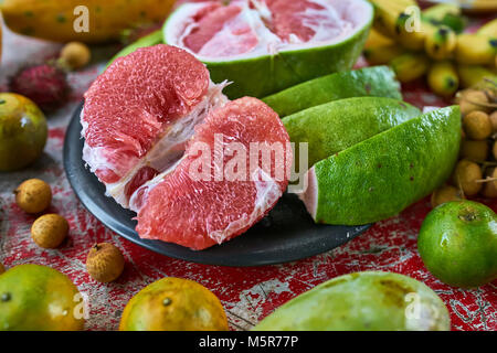 De délicieux fruits exotiques sur la table rouge en bois miteux. Il y a une menuiserie pomelo sur la plaque noire, agrumes, litchis, papayes, ramboutans et les bananes. Cl Banque D'Images