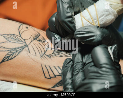 Tatoueur au travail. Woman in Black tatouage gants en latex d'un jeune homme à la main avec image colorée en studio. Close up. Banque D'Images