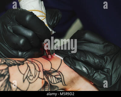 Tatoueur au travail. Woman in Black tatouage gants en latex d'un jeune homme à la main avec image colorée en studio. Close up. Banque D'Images