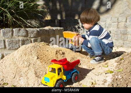 Petit garçon de trois ans jouant dans le sable avec une pelle et camion. Banque D'Images