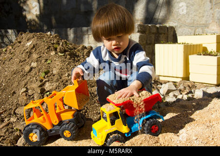 Petit garçon de trois ans jouant dans le sable avec une pelle et camion. Banque D'Images