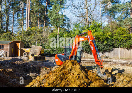 Grosse orange plante lourde mechanical digger garé sur un chantier de fouilles après avoir creusé pour les fondations d'un nouveau développement résidentiel Banque D'Images