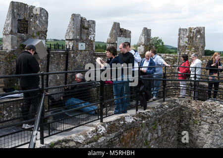 Une longue file de visiteurs regarder une des visiteurs établir avec l'aide d'un membre du personnel du château de la baiser la pierre de Blarney en haut de Banque D'Images