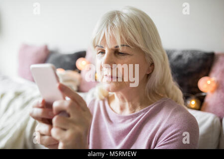 Portrait de senior lady using smartphone assis à la maison Banque D'Images