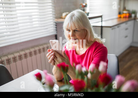 Portrait of senior dame assis à table de cuisine à l'aide de mobile Banque D'Images