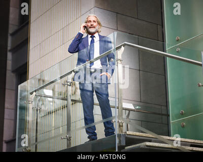 Directeur général de race blanche debout sur haut des escaliers d'effectuer un appel en utilisant votre téléphone mobile en immeuble de bureaux modernes, low angle view. Banque D'Images